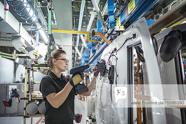 Female worker assembling car doors on production line in a car factory