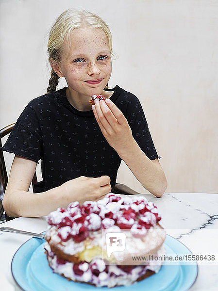 Mädchen isst ihren selbstgebackenen Kuchen mit frischen Himbeeren am Küchentisch  Porträt