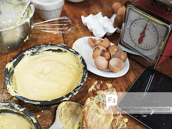 Messy baking preparation on kitchen table with cake mixture  kitchen scales  kitchen utensils and digital tablet