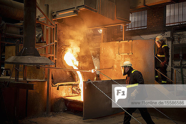 Workers pouring liquid titanium alloy from furnace in titanium recycling plant