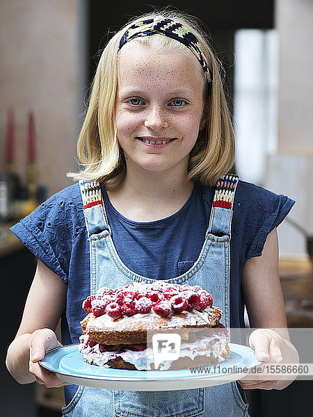 Mädchen beim Backen eines Kuchens  hält in der Küche hausgemachten Kuchen mit Himbeeren oben drauf  Portrait