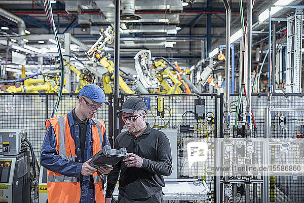 Apprentice engineer with mentor programming robots in car factory