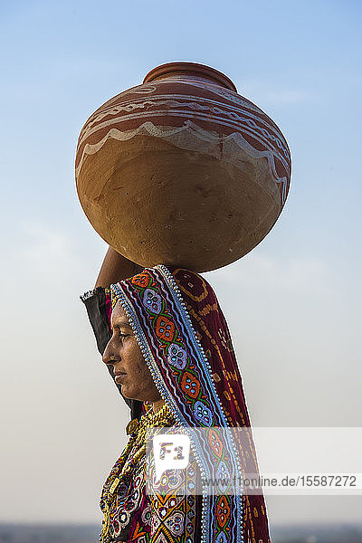 Ahir-Frau in traditioneller bunter Kleidung  die Wasser in einem Tonkrug auf dem Kopf trägt  Great Rann of Kutch Desert  Gujarat  Indien