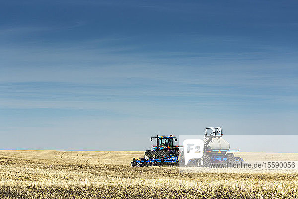 Tractor with air seeder in field with blue sky and hazy clouds  near Beiseker; Alberta  Canada