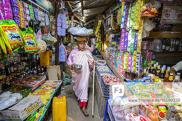 Buddhistische Nonne beim Einkaufen auf einem Markt  die Gegenstände in einem Korb auf dem Kopf trägt; Bagan  Mandalay-Region  Myanmar