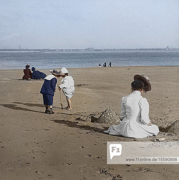 Magic Lantern slide circa 1880  Victorian/Edwardian  social history. Beach scene with children playing and adults sitting in the sun. The children have built a sandcastle.