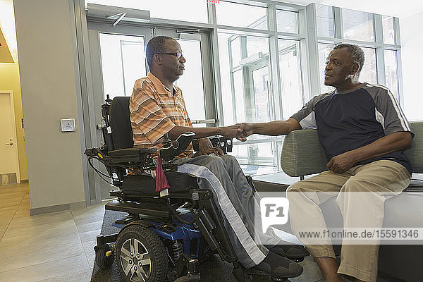 Man with Guillain-Barre Syndrome on power chair doing a handshake with his father in living room