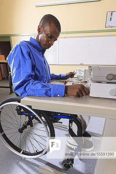Ingenieurstudent in einem Elektronikunterrichtsraum  der wegen einer Rückenmarkshautentzündung im Rollstuhl sitzt und ein Prototyping-Breadboard vorbereitet
