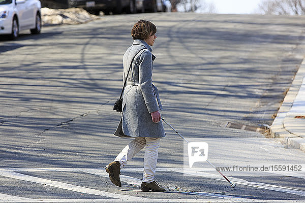 Junge blinde Frau  die mit ihrem Stock die Straße überquert