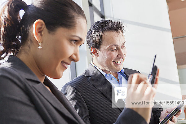 Geschäftspaar im Büro mit Blick auf Tablet und Smartphone
