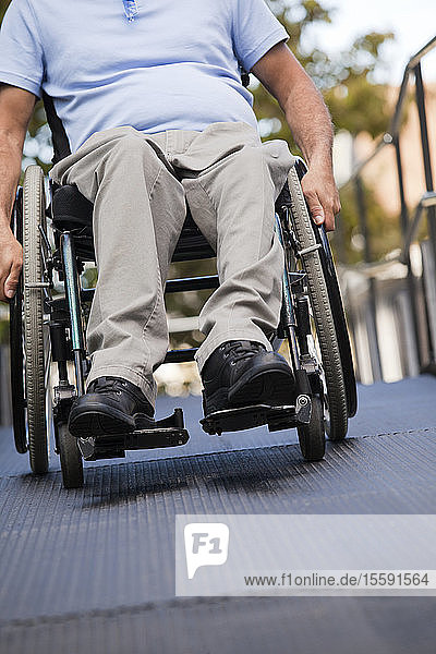 Mann mit Rückenmarksverletzung im Rollstuhl fährt eine Rollstuhlrampe im Freien hinauf