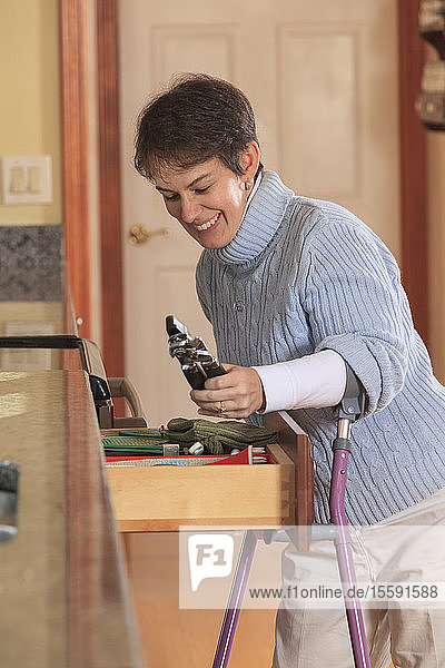 Woman with Cerebral Palsy using crutches and opening a drawer in her kitchen