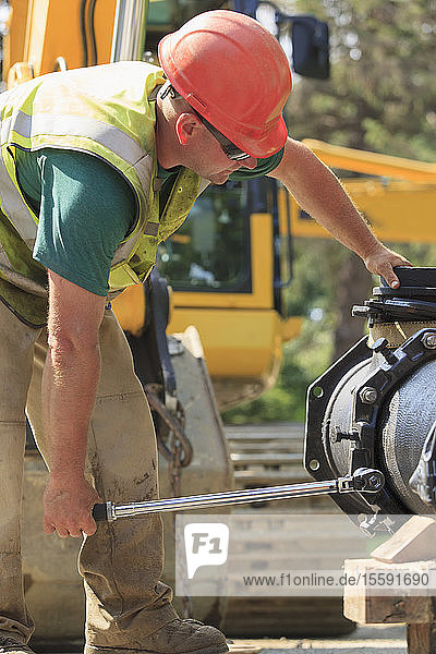 Ein Bauarbeiter verwendet einen Drehmomentschlüssel  um einen Wasserleitungsabschnitt mit Schrauben zu sichern.
