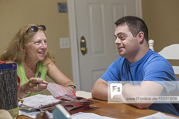 Mann mit Down-Syndrom sitzt neben seiner Mutter und bezahlt Rechnungen