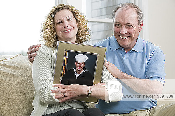 Portrait of a mature couple holding picture of their son working in the military.
