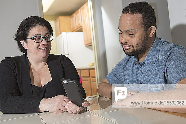 African American man with Down Syndrome using a cell phone with his mother at home