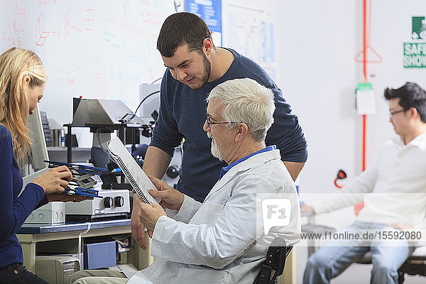 Professor with muscular dystrophy and engineering students using manual to set up x-ray fluorescence experiment in a Laboratory