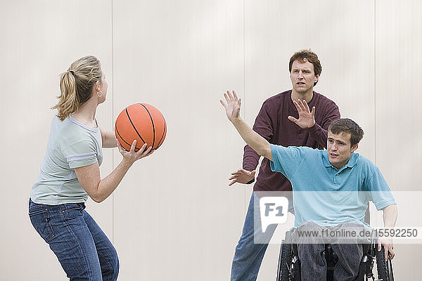 Junger Mann sitzt im Rollstuhl und spielt Basketball.