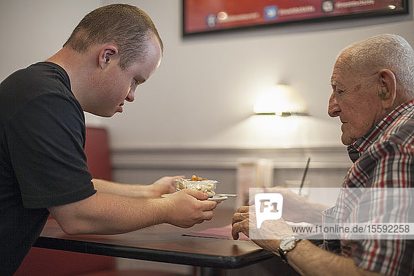 Kellner mit Down-Syndrom serviert einem Kunden in einem Restaurant das Essen
