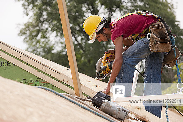 Ein spanischer Zimmermann arbeitet mit einer Kreissäge auf dem Dach eines im Bau befindlichen Hauses