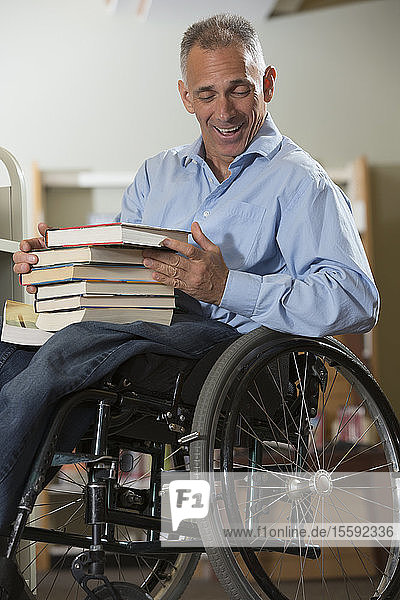 Mann im Rollstuhl mit einer Rückenmarksverletzung lässt Bücher aus einem Regal in einer Bibliothek fallen