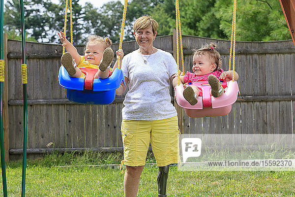 Grandmother with a prosthetic leg playing on a swing set with her grandchildren
