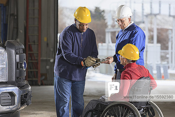 Kfz-Techniker in einer Kraftwerkswerkstatt beim Abzeichnen eines Arbeitsprotokolls  Vorgesetzter im Rollstuhl