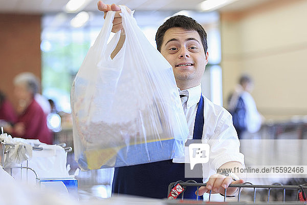 Mann mit Down-Syndrom hält eine Tüte  während er in einem Lebensmittelladen arbeitet