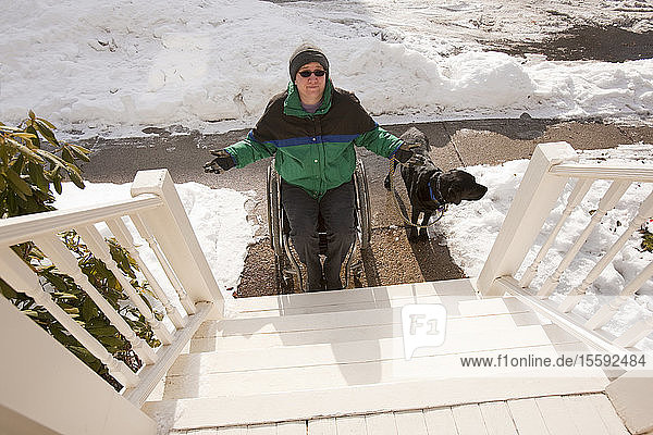 Frau mit Multipler Sklerose versucht  mit einem Diensthund eine Treppe hinaufzusteigen