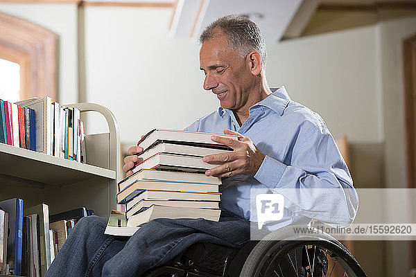 Mann im Rollstuhl mit einer Rückenmarksverletzung wählt Bücher aus einem Regal in einer Bibliothek aus