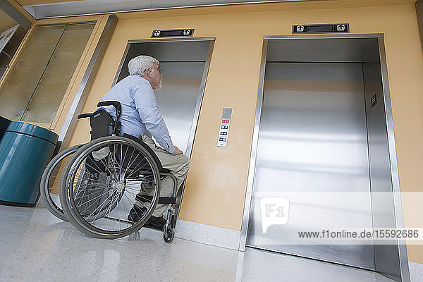 Universitätsprofessor mit Muskeldystrophie im Rollstuhl beim Warten auf einen Aufzug