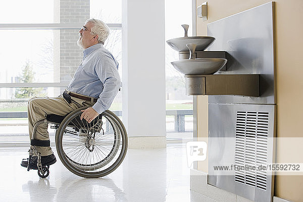 Universitätsprofessor mit Muskeldystrophie im Rollstuhl in einem Korridor