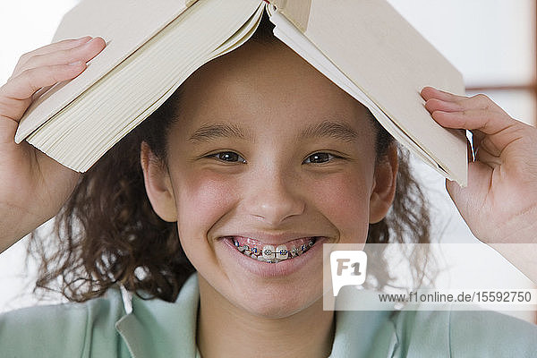 Porträt eines hispanischen Mädchens  das sich ein Buch auf den Kopf legt und lächelt
