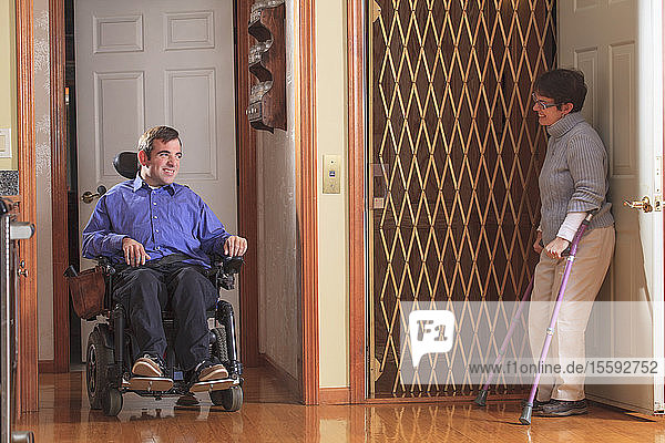 Frau mit Cerebralparese hilft Mann mit Cerebralparese im motorisierten Rollstuhl in den Hausaufzug