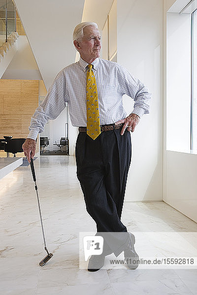View of a businessman with golf club standing in an office.