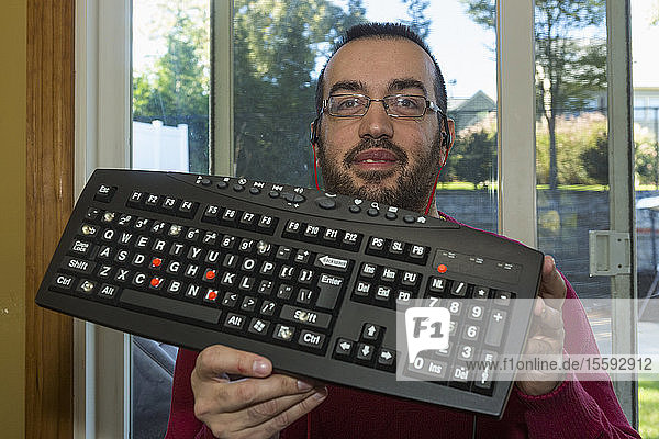 Mann mit Sehbehinderung hält seine Tastatur hoch  die ihn hören lässt