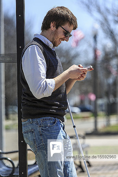 Young blind man at a bus stop using assistive technology