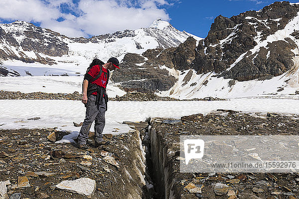 A hiker peers into a crevasse on Castner Glacier in the Alaska Range with Black Cap in the background; Alaska  United States of America