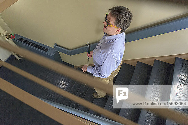 Mann mit angeborener Blindheit benutzt seinen Stock  um eine Treppe hinunterzugehen