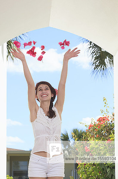 Lächelnde junge Frau wirft Blumenblätter in die Luft