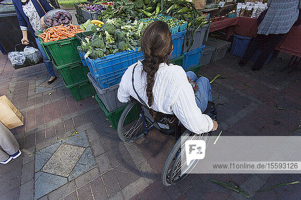 Frau mit Rückenmarksverletzung im Rollstuhl beim Einkaufen auf dem Wochenmarkt