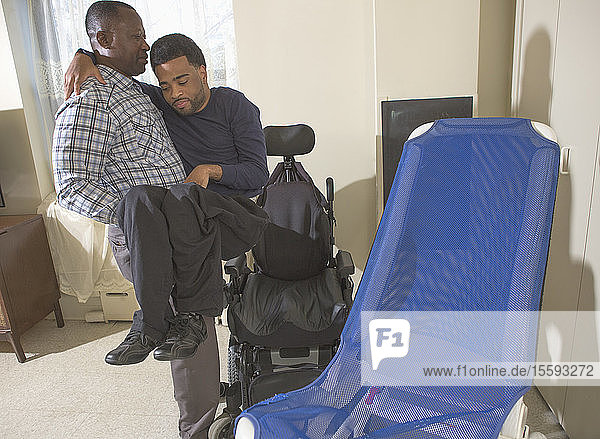African American man with Cerebral Palsy with his Personal Care Assistant helping him into his wheelchair at home
