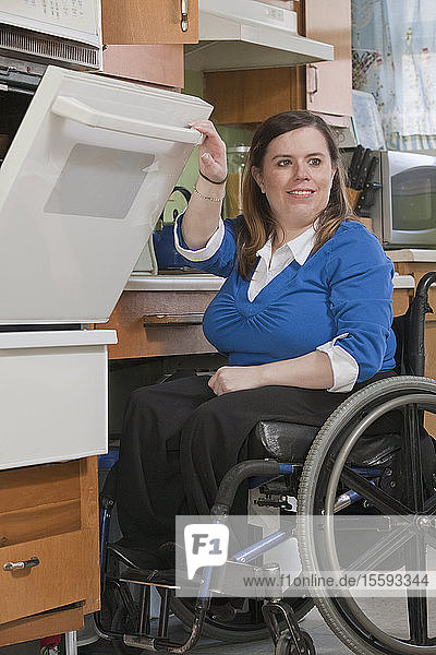 Frau mit Spina Bifida im Rollstuhl benutzt einen Herd in der barrierefreien Küche