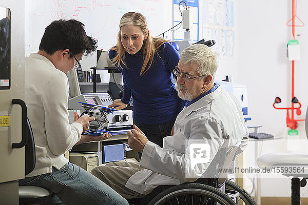 Professor with muscular dystrophy working with engineering students setting up adjustable stage at chemical analysis instrument in a laboratory