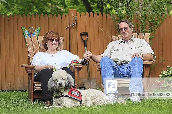 Frau mit RSD und ihr Diensthund mit Ehemann sitzen in ihrem Garten und halten sich an den Händen