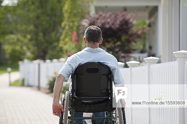 Mann mit Querschnittslähmung im Rollstuhl auf einem Vorstadtspaziergang mit Häusern