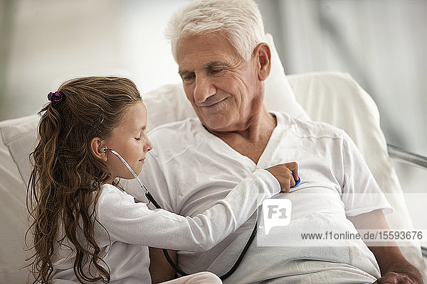 Älterer Mann erhält im Krankenhaus Besuch von seiner Enkelin  die mit einem Stethoskop spielt