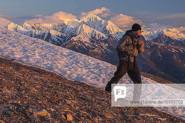 Ein Wanderer überquert einen Berghang in der Alaska Range bei Sonnenaufgang; Alaska  Vereinigte Staaten von Amerika
