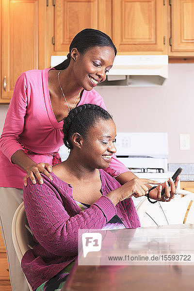 Two sisters looking at a smartphone in the kitchen  one with learning disability
