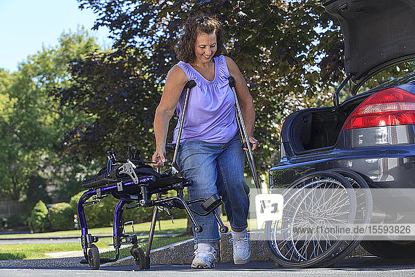 Frau mit Spina Bifida benutzt Krücken  um den Rollstuhl für die Fahrt im Auto zu zerlegen